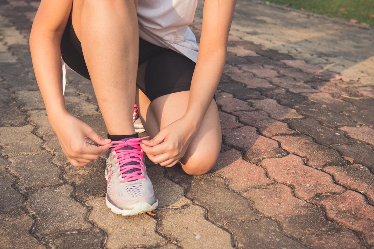 Adult woman tying pink laces on running shoes outdoors. Focuses on fitness and lifestyle.